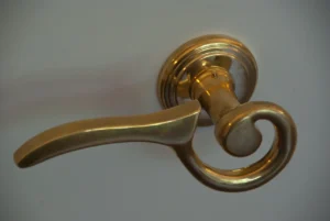 Manivela decorativa de latón dorado con diseño de voluta instalada sobre una puerta de interior blanca lacada.
